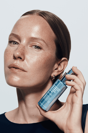 Woman holding a blue skincare bottle against a light background